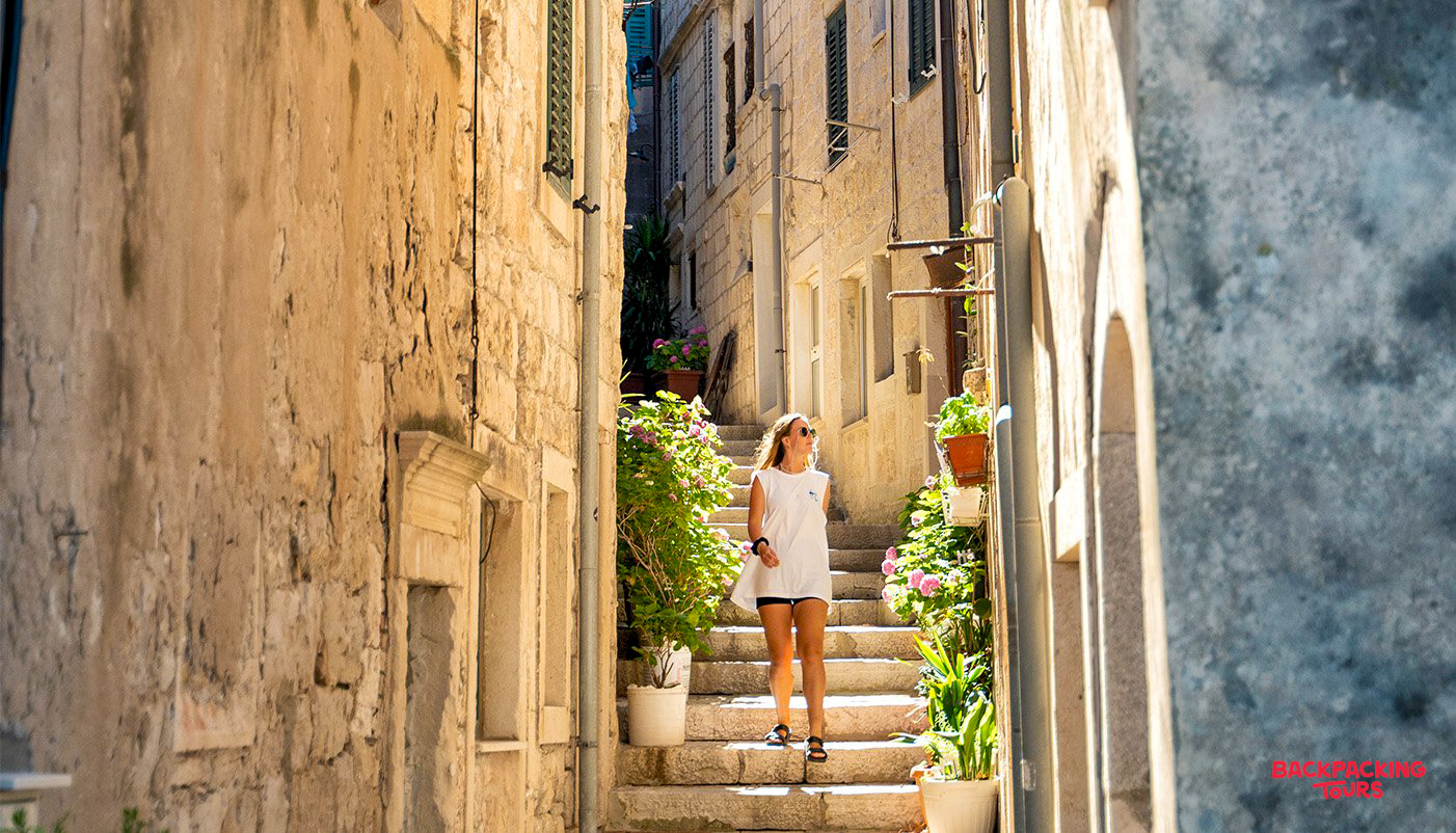 A woman explores the charming, sunlit stone laneways and steps of Korcula Old Town.