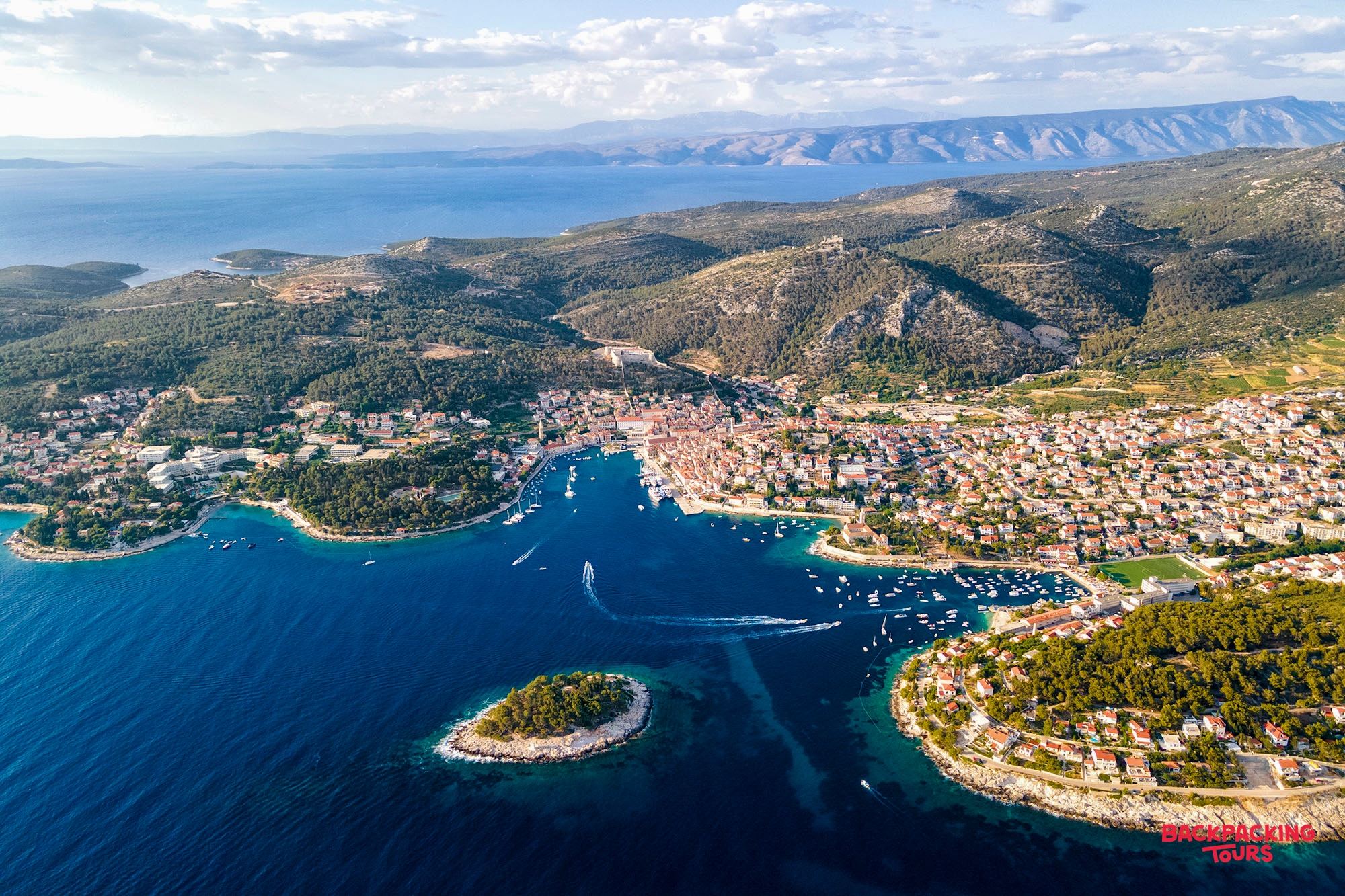 Hvar's vibrant harbor, teeming with boats, surrounded by charming buildings and lush green hills.
