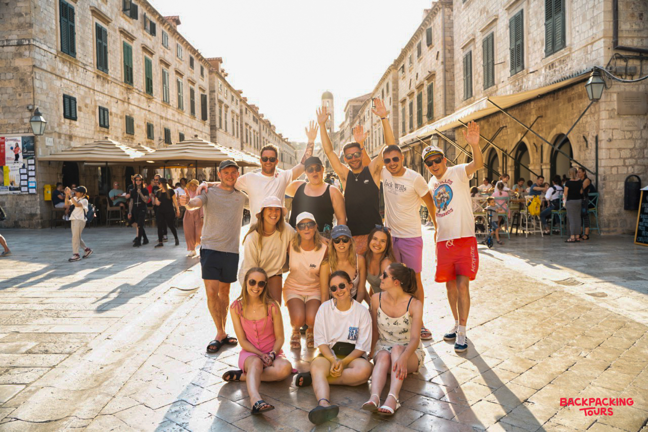 A joyful group of backpackers poses on the sun-drenched, cobbled streets of Dubrovnik's Old Town.