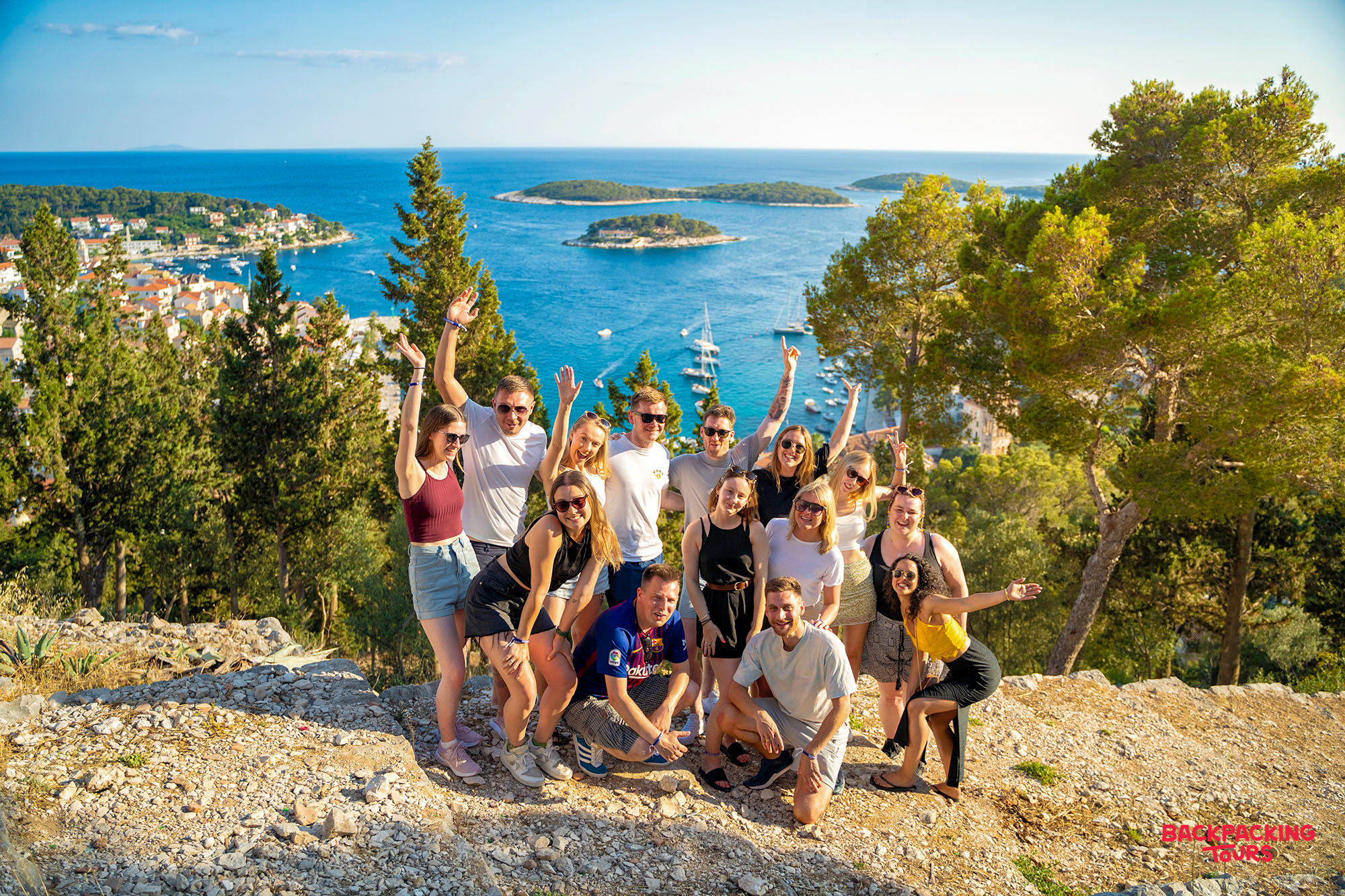 Travelers wave from a Hvar viewpoint, enjoying stunning views of the town and islands.