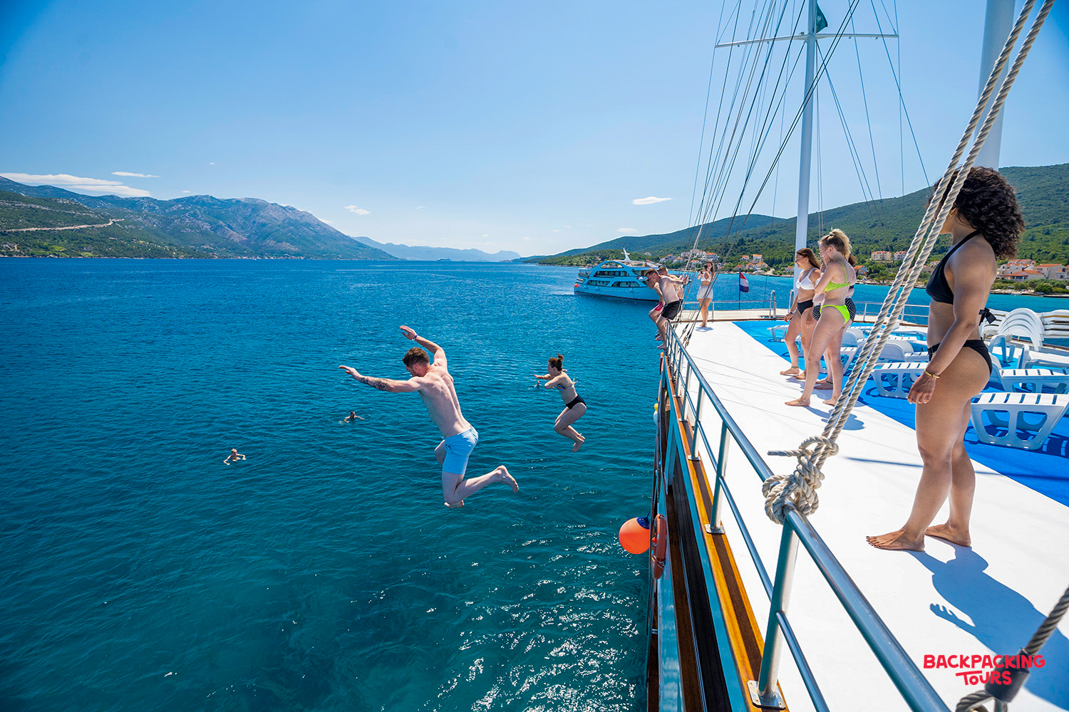 Travelers joyfully jump from a boat into the clear blue Adriatic Sea off the coast of Croatia.