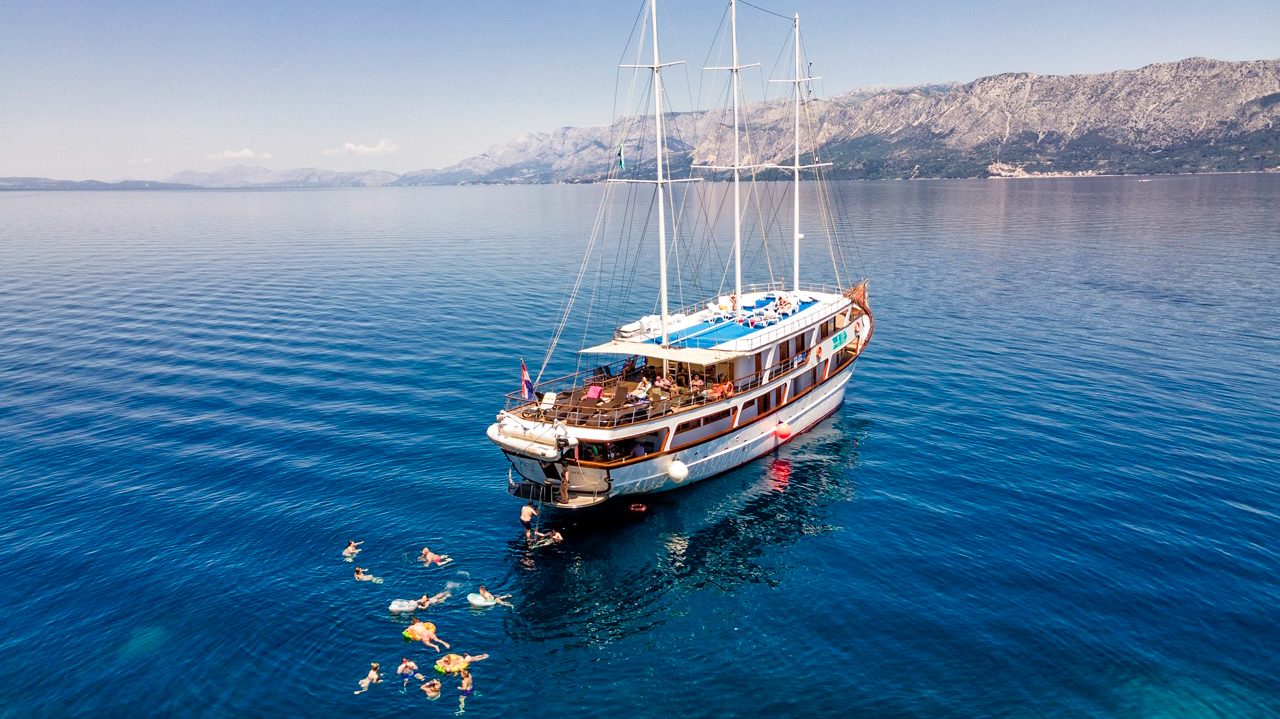People swim and snorkel in the clear blue sea next to a large sailing boat in Croatia.