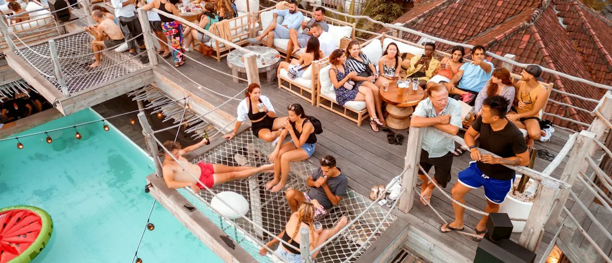 Many people socialising and relaxing at a multi-level outdoor venue with a swimming pool.