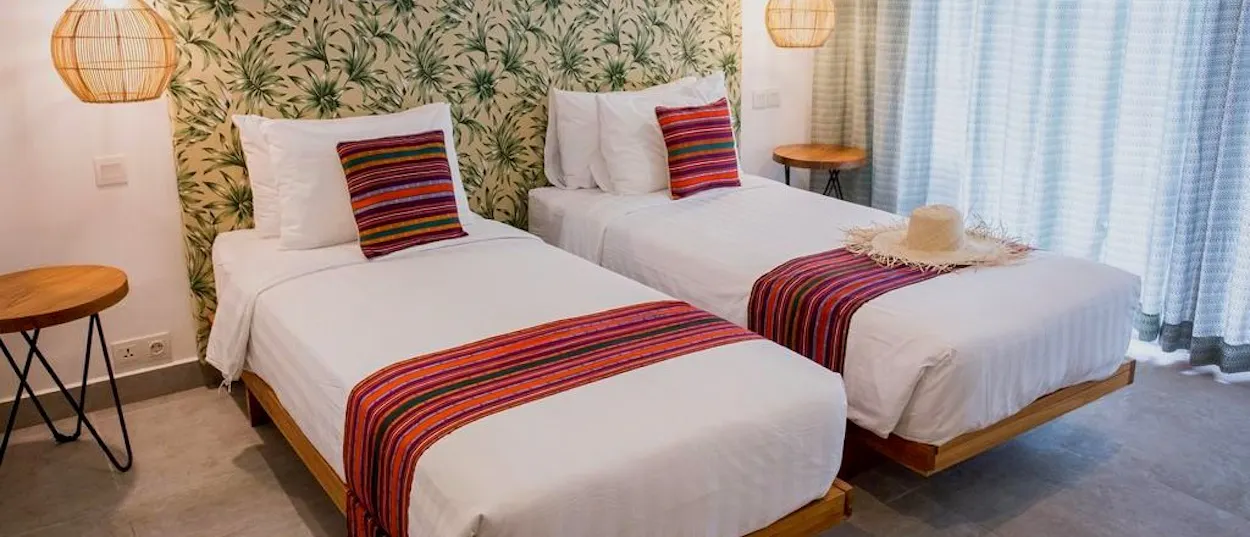 Two single beds with white linen, colourful runners, and leaf-patterned headboards in a bright room.