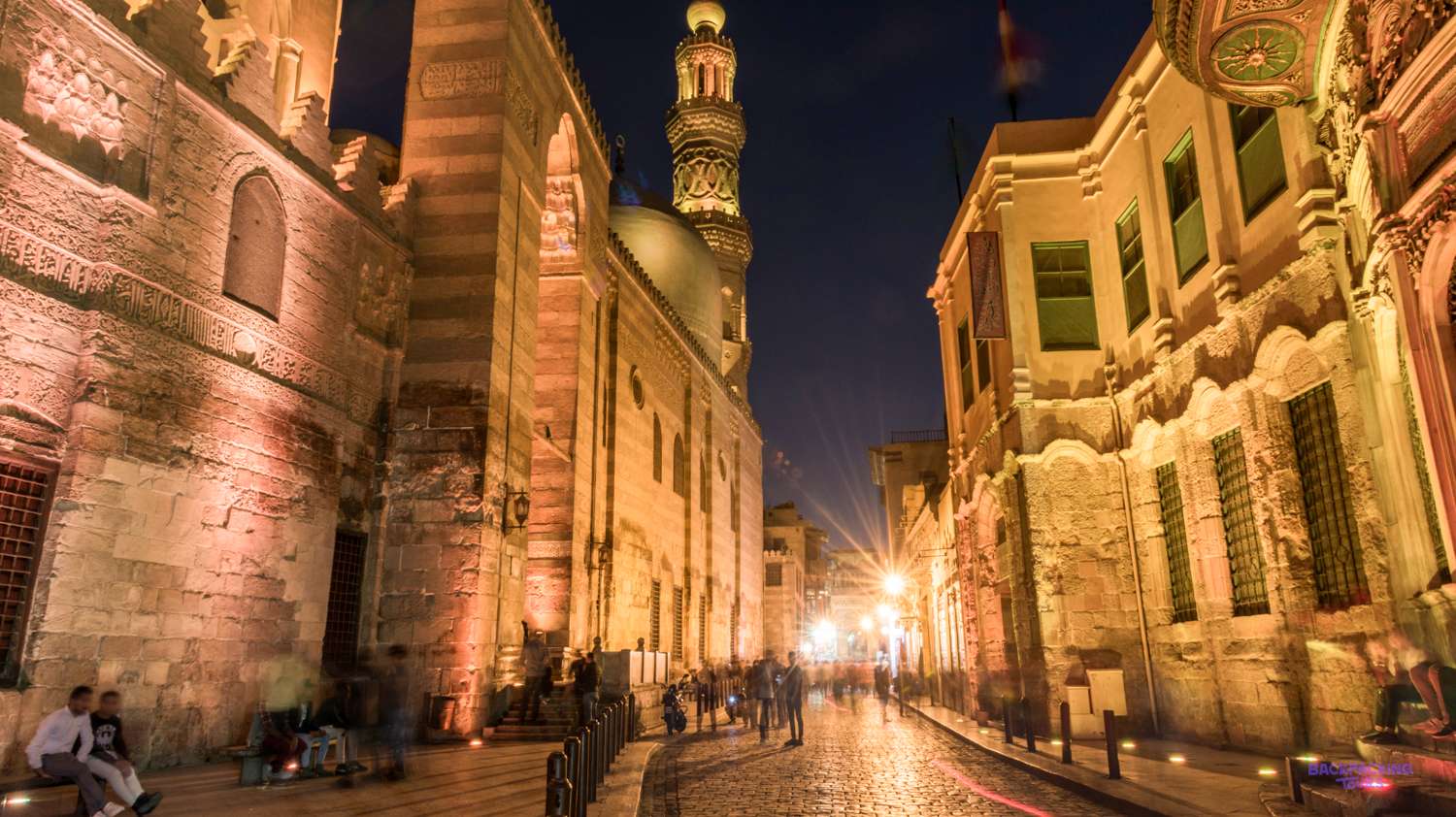 A lively historic street in Cairo at night, with a minaret and people under warm lights.