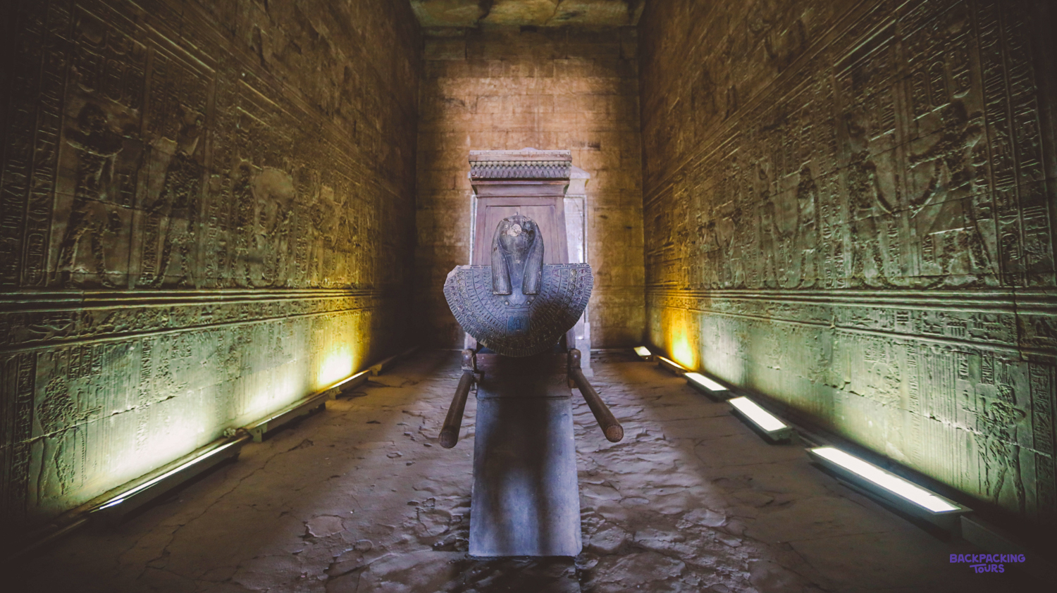 A majestic stone statue stands illuminated in the ancient Edfu Temple, walls covered in intricate hieroglyphs.