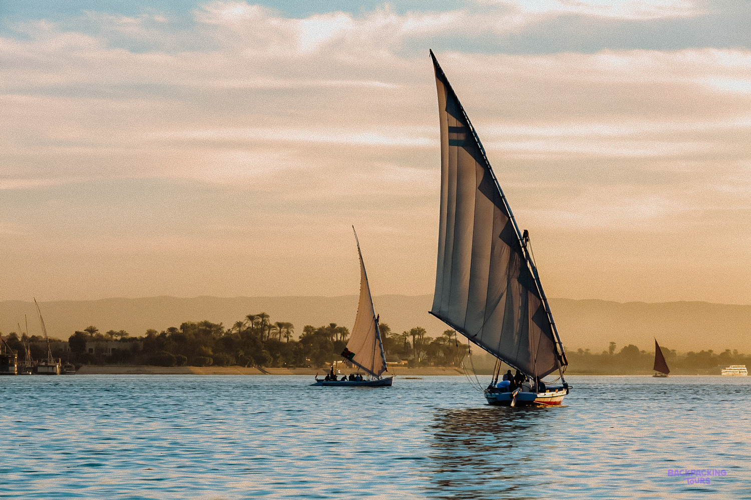 Traditional feluccas sail gracefully on the Nile River near Luxor under a beautiful golden sky.