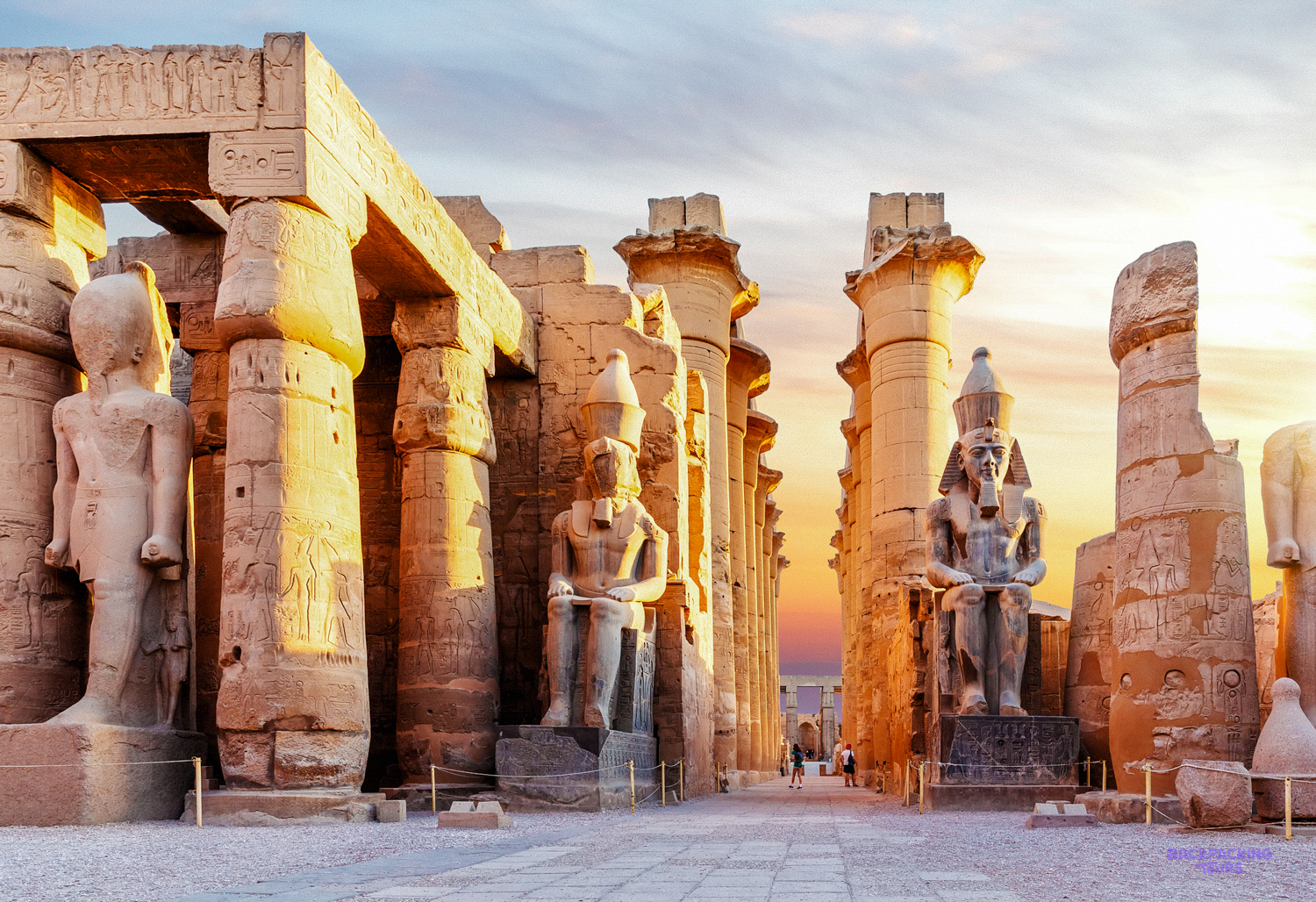 Colossal statues and towering columns of Luxor Temple bathed in the warm glow of the setting sun.