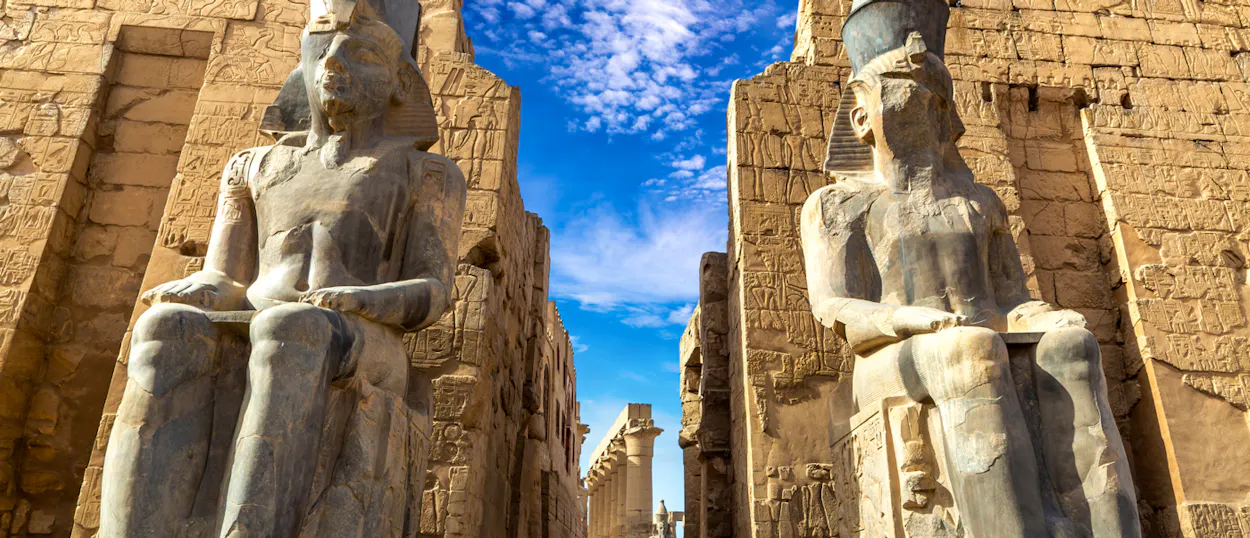 Two colossal seated pharaoh statues guard the entrance to an ancient temple in Luxor, Egypt.