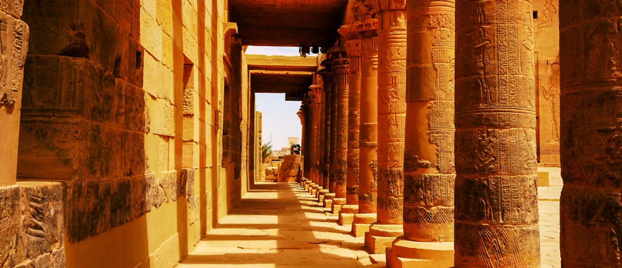 A long corridor of ancient carved pillars at Philae Temple in Aswan, Egypt.