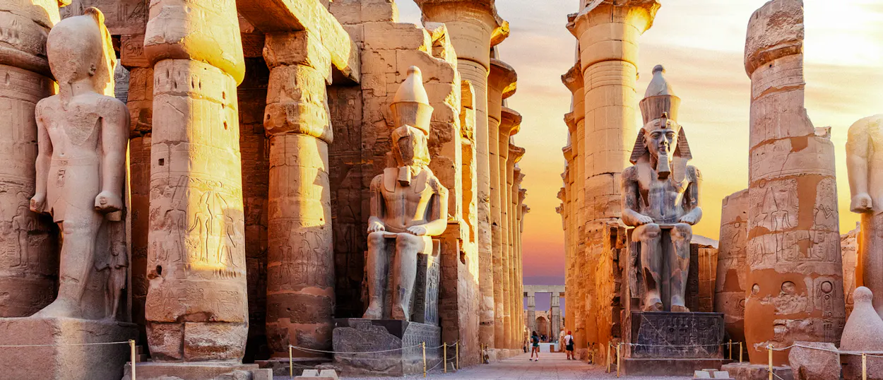 Colossal ancient Egyptian statues and massive columns glow in the warm light of Luxor.