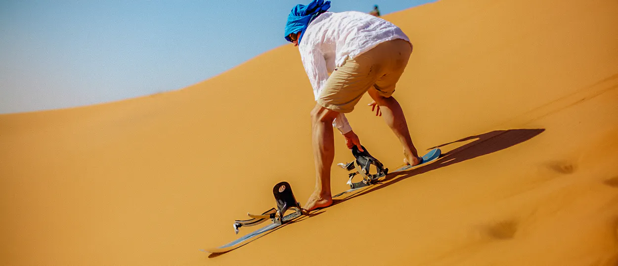 An adventurous person sandboarding down a vast golden dune in the Wadi al Hitan desert.