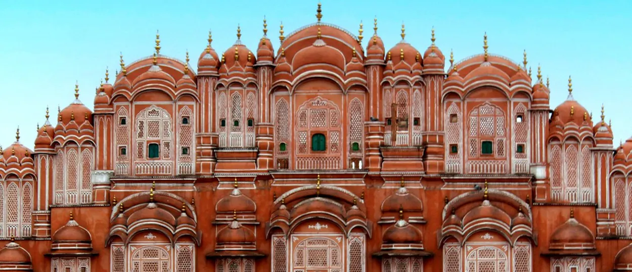 A grand, red-orange palace with many small, intricately carved windows and domed rooftops.