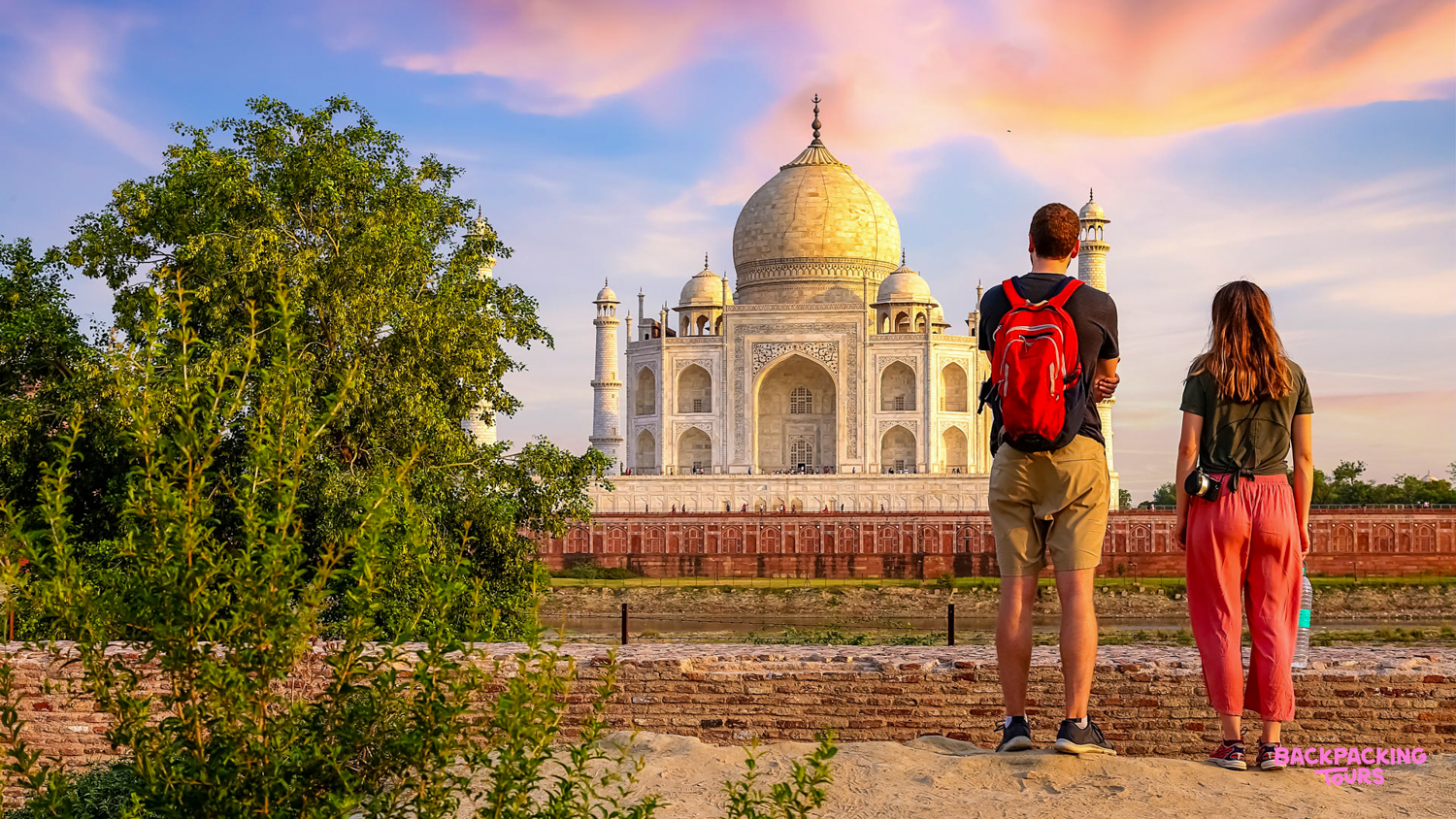 Two backpackers admire the majestic Taj Mahal at sunrise, its white marble glowing in Agra.