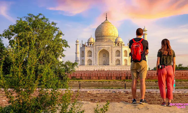 Two backpackers admire the majestic Taj Mahal at sunrise, its white marble glowing in Agra.