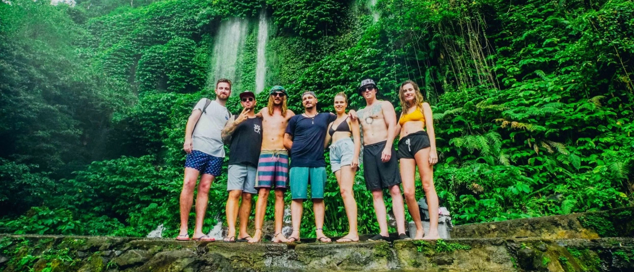 Seven happy friends pose together in front of a magnificent jungle waterfall in Lombok.