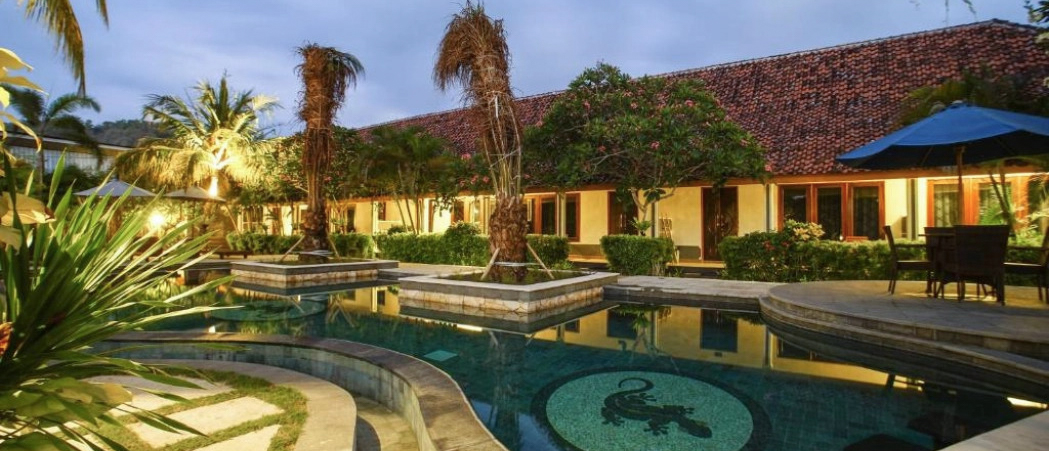 Tropical resort pool in Lombok at twilight, featuring a lizard mosaic and warm lighting.