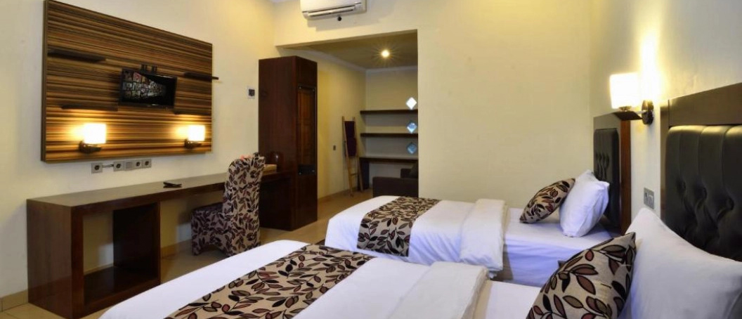 A comfortable hotel room with two beds, a desk, and a TV in Lombok, Indonesia.