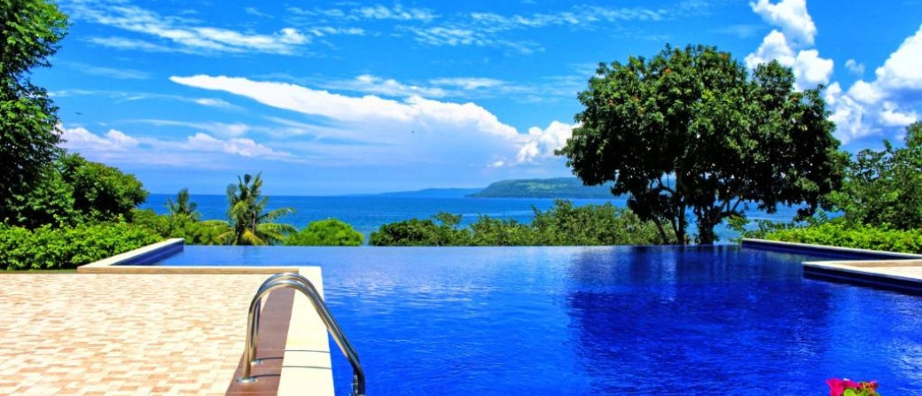 Relaxing infinity pool with vibrant blue water, tropical trees, and ocean views in Sumbawa.