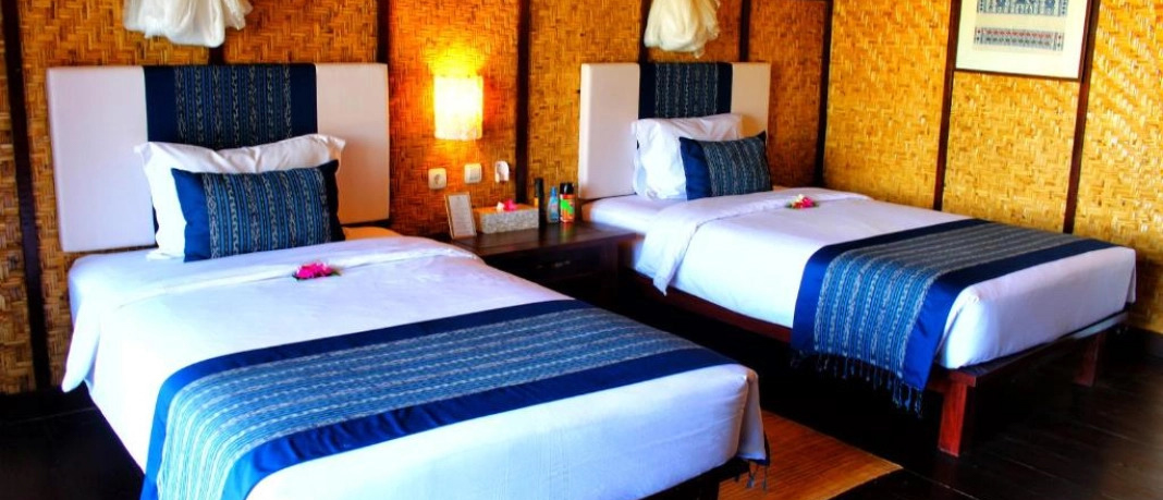 Two cozy single beds with blue runners and woven walls in a hotel room in Sumbawa.