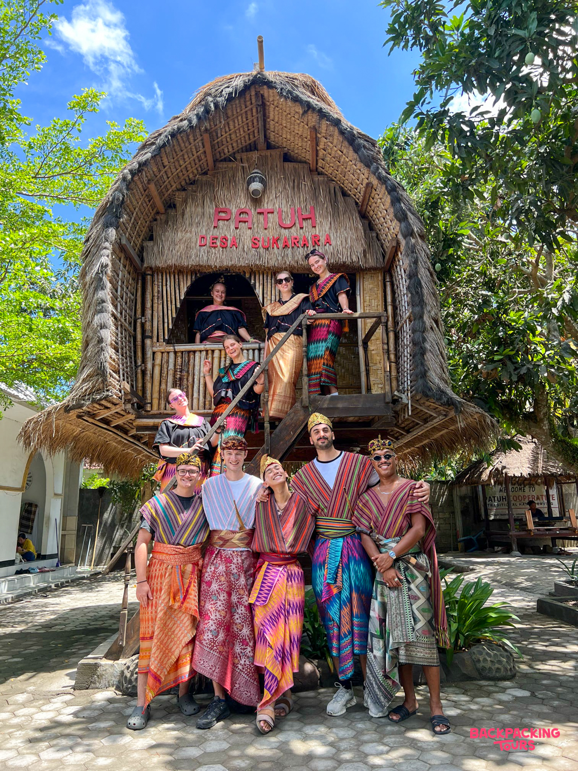 A group of happy travelers wearing colorful traditional Sasak clothing pose at Desa Sukarara village, Lombok.
