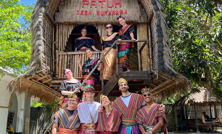 A group of happy travelers wearing colorful traditional Sasak clothing pose at Desa Sukarara village, Lombok.