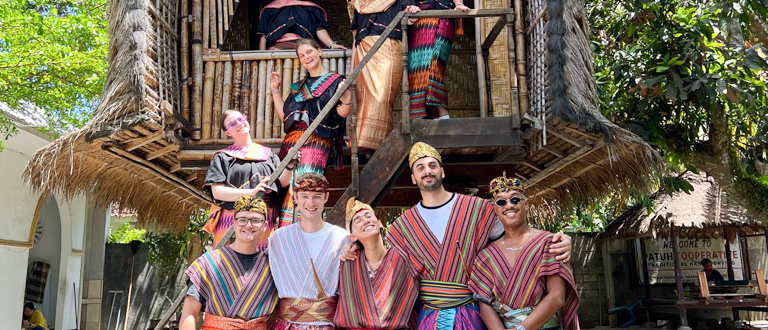 Smiling travelers in colorful traditional clothing pose at a Sasak village in Lombok.