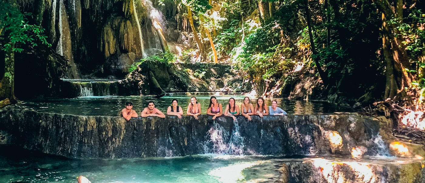 A group of happy travelers relax in a stunning natural waterfall pool on Moyo Island.