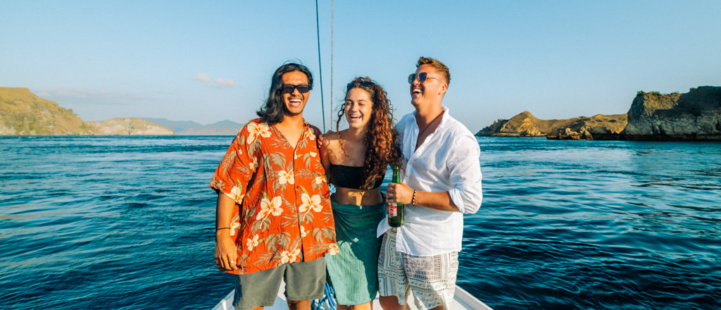Three cheerful friends enjoy sailing on a boat with scenic islands in the background near Satonda.