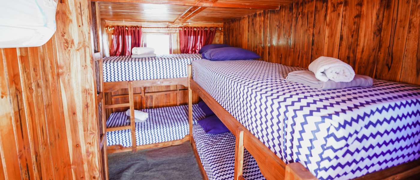 Inside a traditional wooden live-aboard boat cabin featuring four bunk beds with blue zigzag sheets.