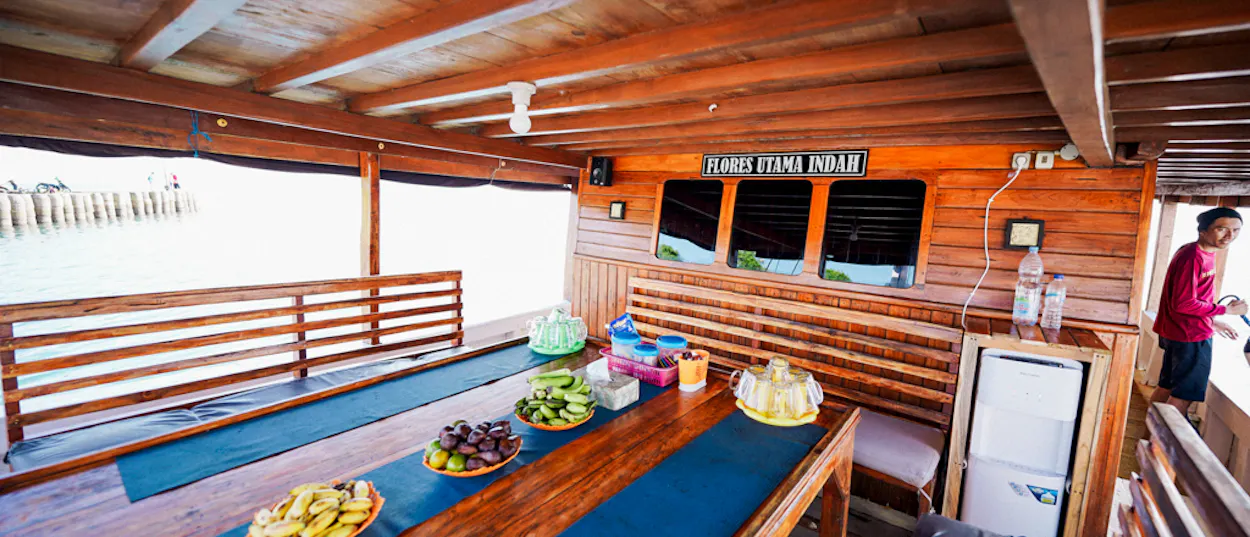 Fresh fruit and snacks await guests on the shaded deck of a traditional wooden live-aboard boat.