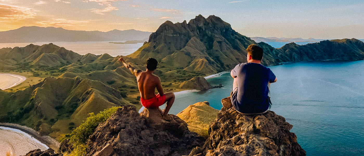 Two men enjoying an epic sunset viewpoint over Padar Island's stunning green hills and bays.