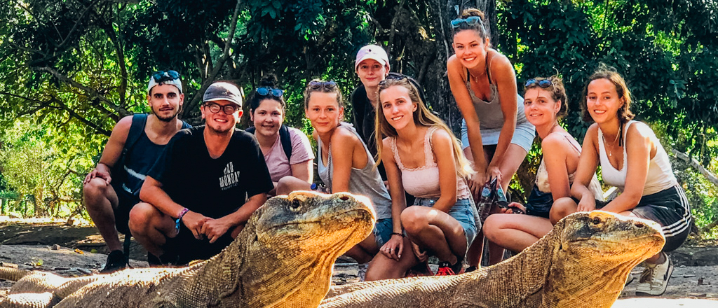Smiling backpackers pose with two large Komodo dragons on Komodo Island, Indonesia.