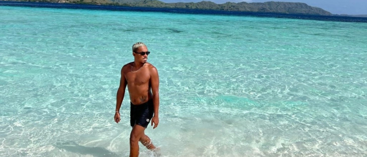 Man with sunglasses walking out of stunning clear turquoise water on a sunny Lombok beach.