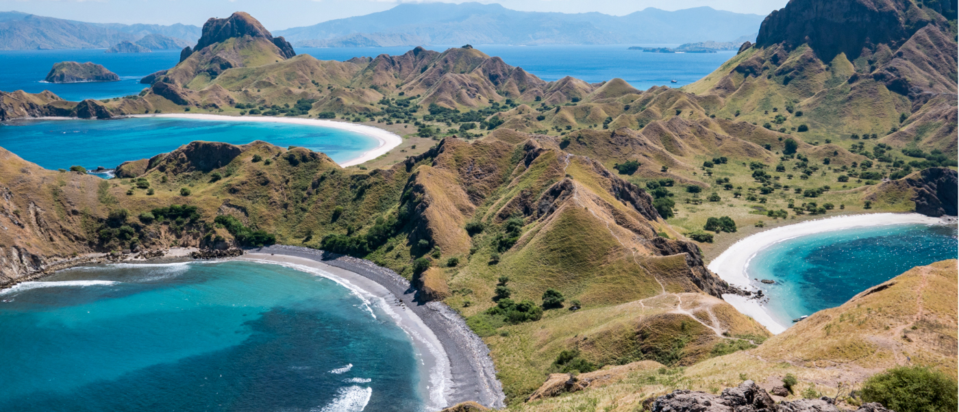 Panoramic view of three crescent beaches with turquoise water nestled between rolling grassy hills on Padar Island.