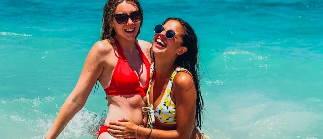 Two happy women in bikinis laughing and embracing in the clear turquoise water of Lombok.