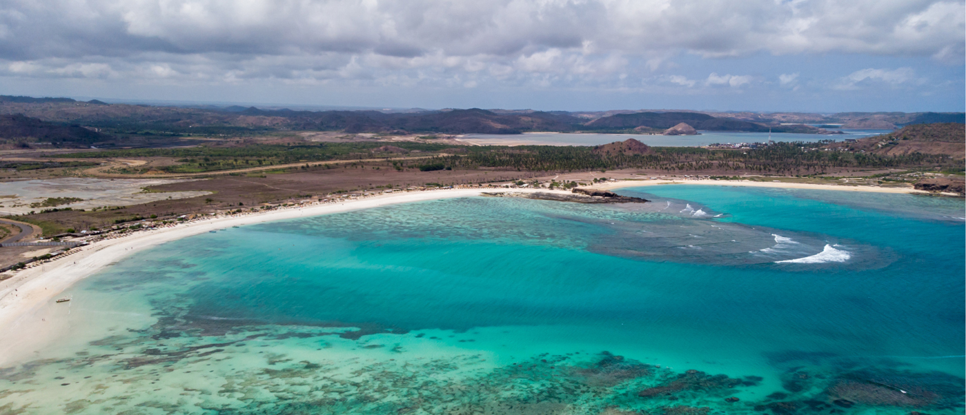 Beautiful curved sandy beach with clear turquoise water and distant hills on Lombok island.