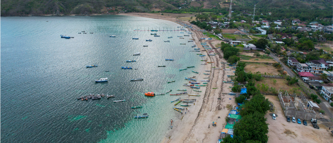 Traditional fishing boats line the clear turquoise waters and sandy beach of Lombok.
