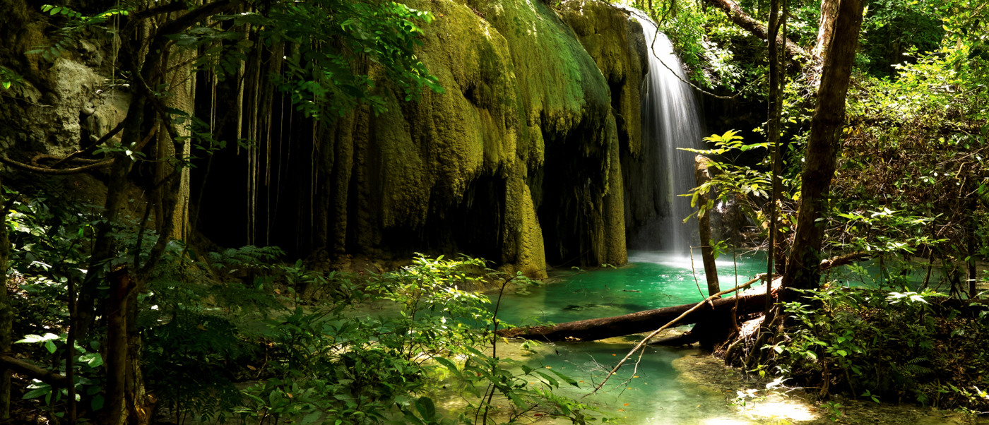 A serene waterfall plunges into a bright turquoise pool, surrounded by lush jungle on Moyo Island.