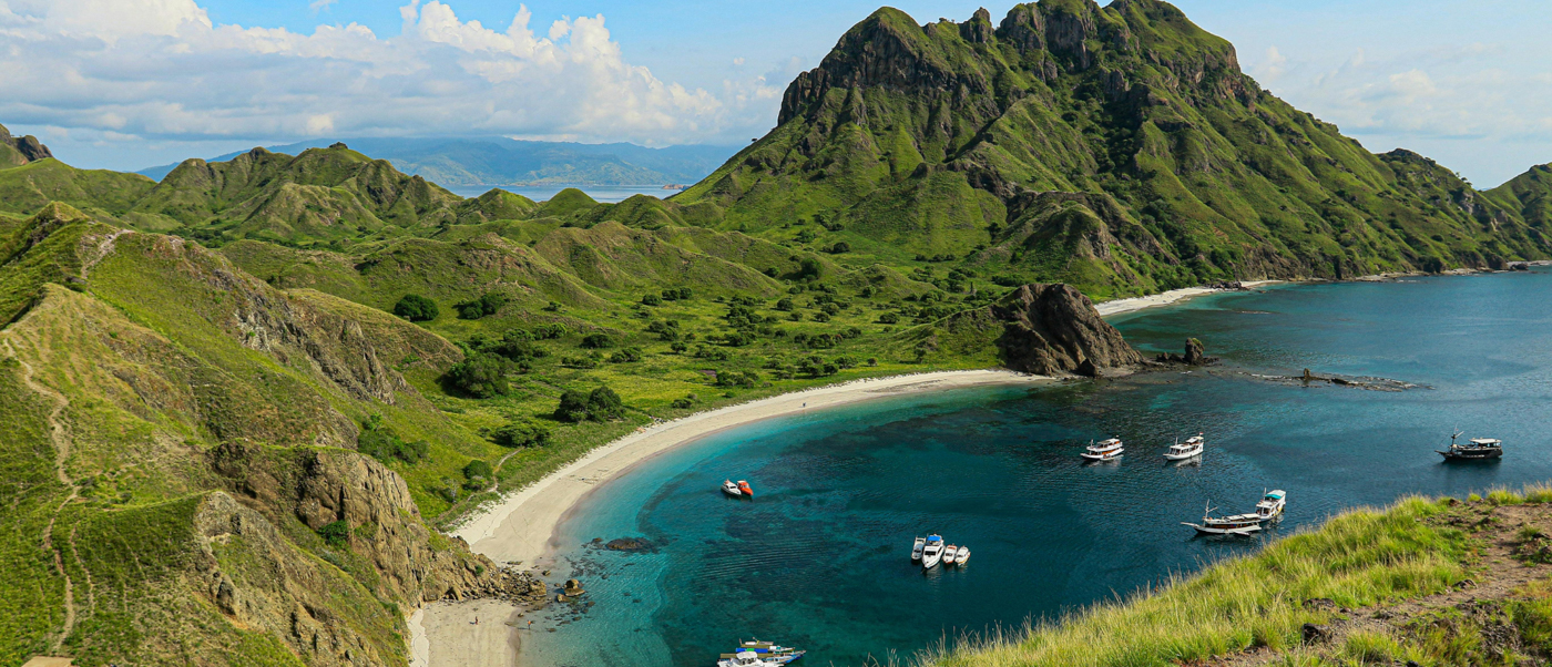 Beautiful bay with a white sand beach, clear turquoise water, and lush green hills.