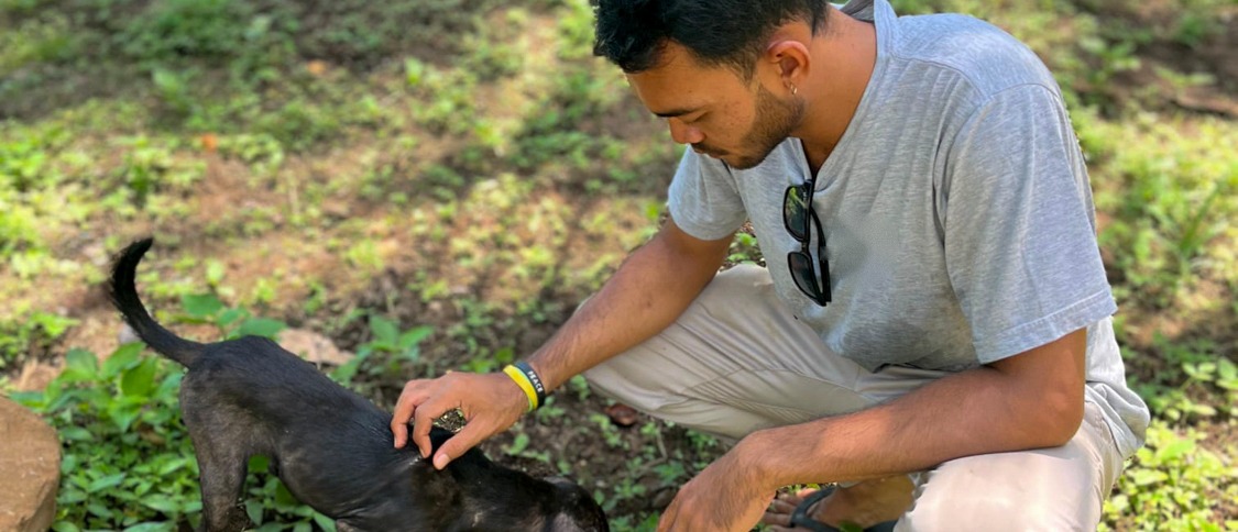 A member of the local team crouches on the grass to feed a black dog from a bowl.