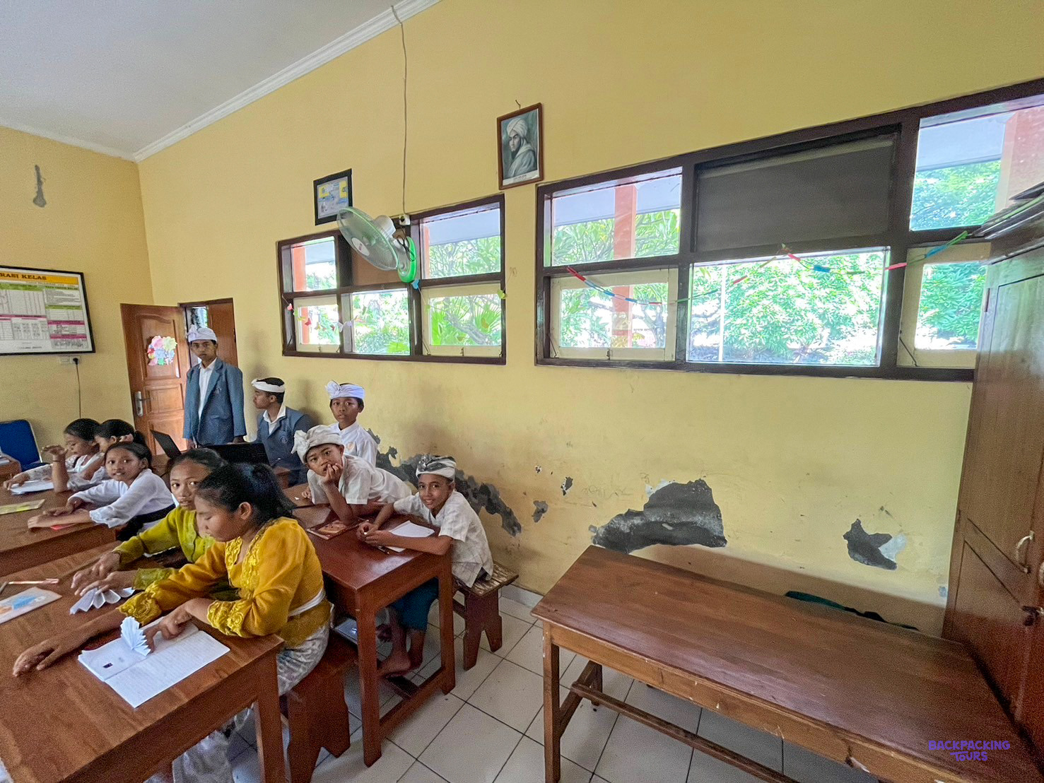 Schoolchildren sit at wooden desks drawing in a classroom with fresh yellow walls.