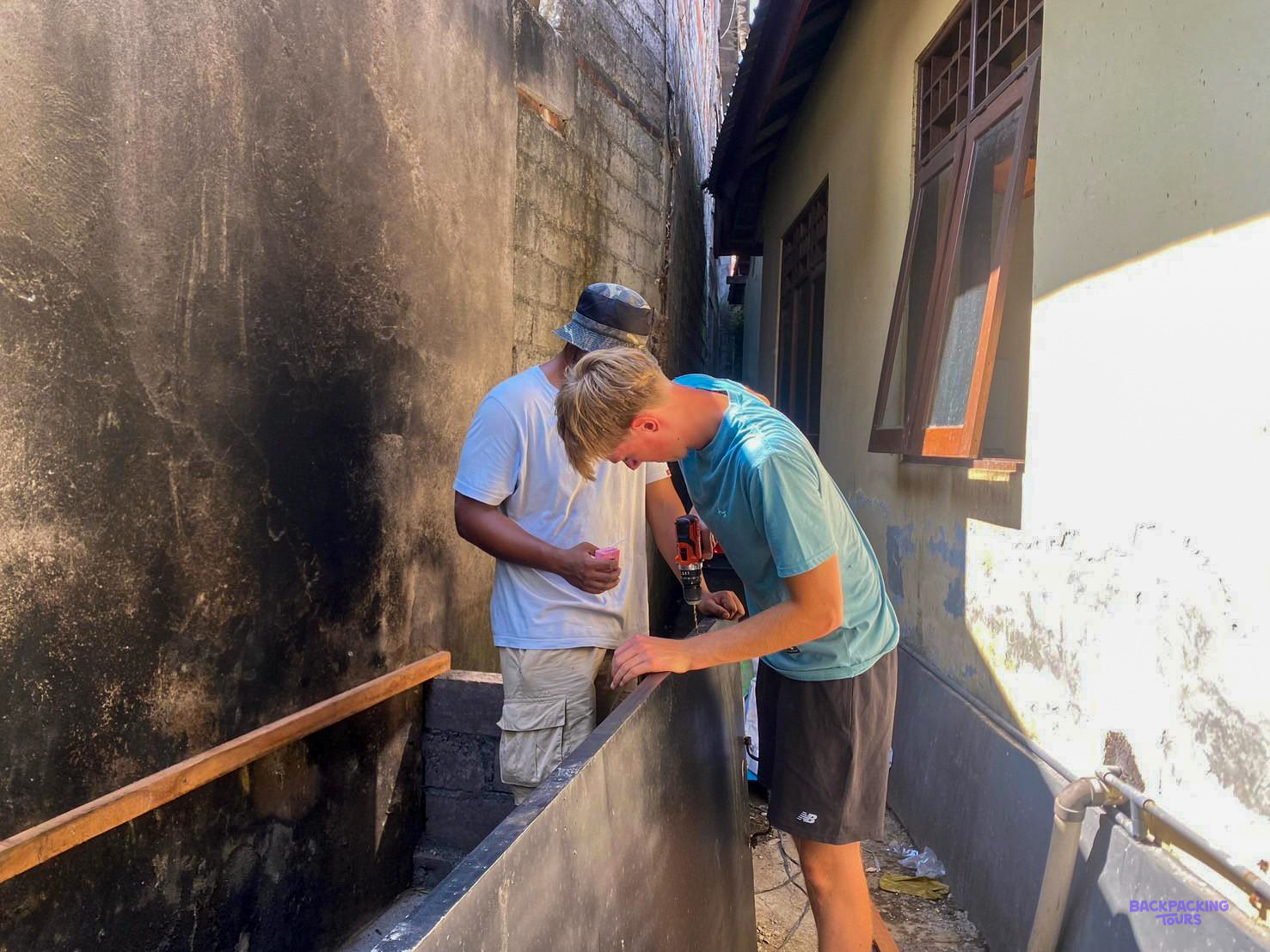 A volunteer drills a board onto a blackened wall as a local builder looks on.