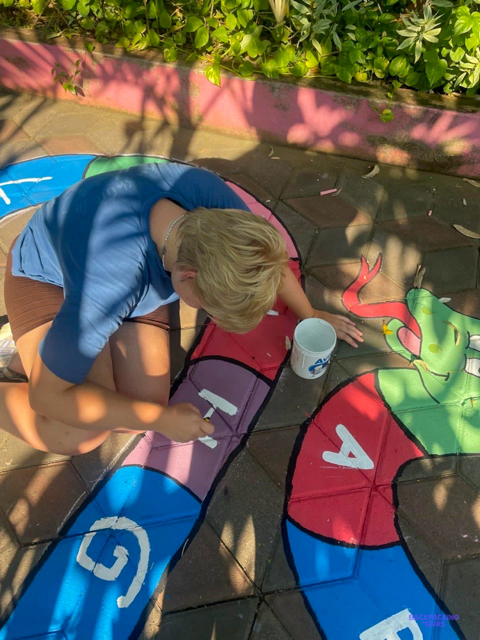 A volunteer paints a colourful hopscotch game onto the playground of a school.