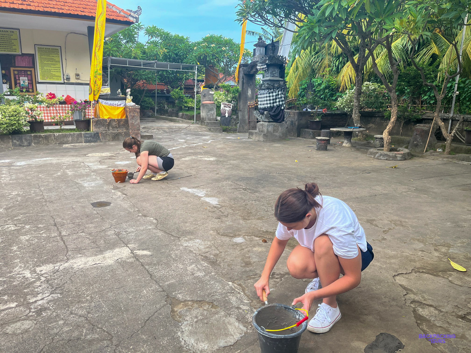 Volunteers kneel with paint buckets to mark out lines on a quiet school courtyard.