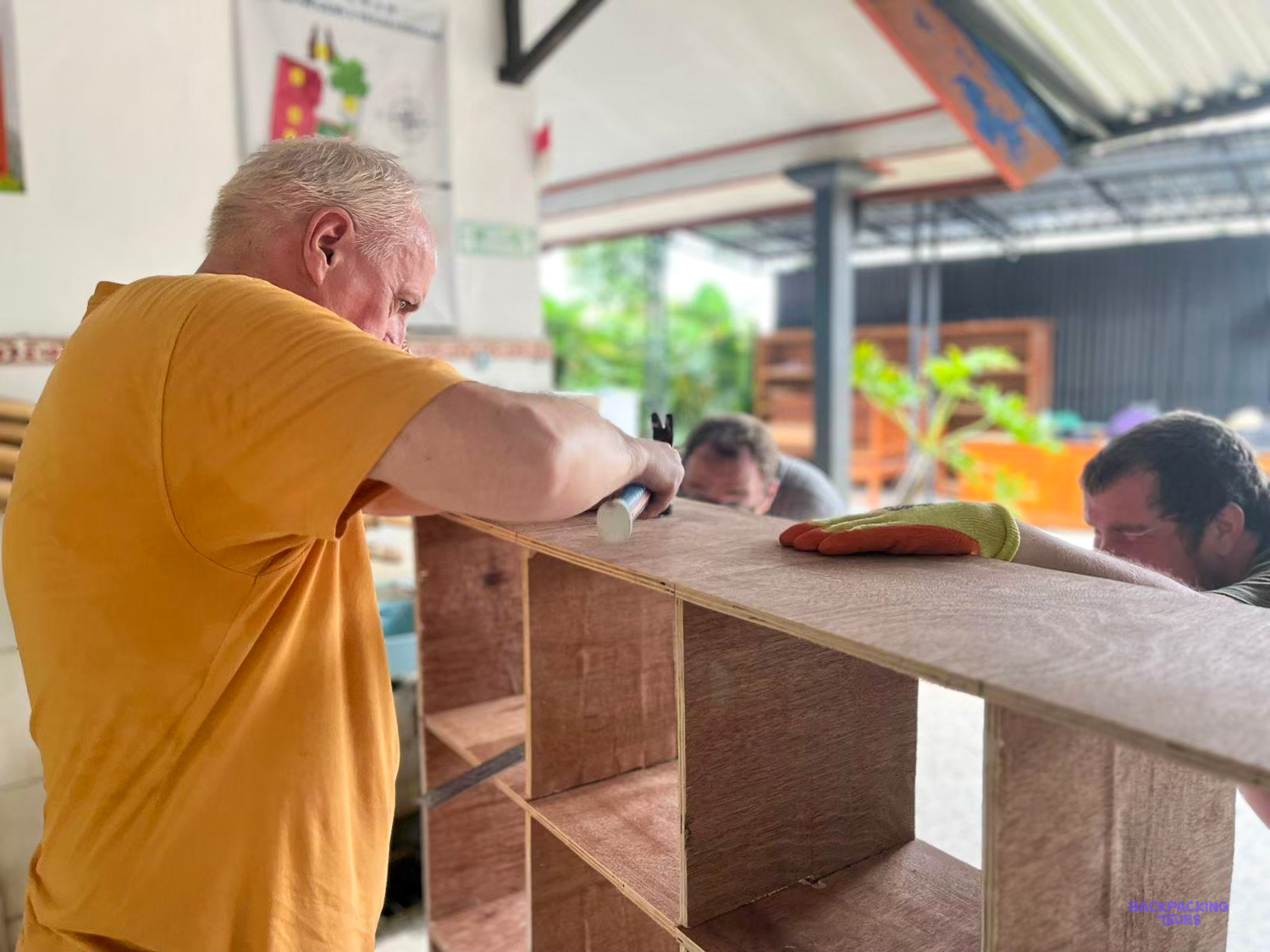 A volunteer sands a set of new wooden shelves with a local builder at the other end.