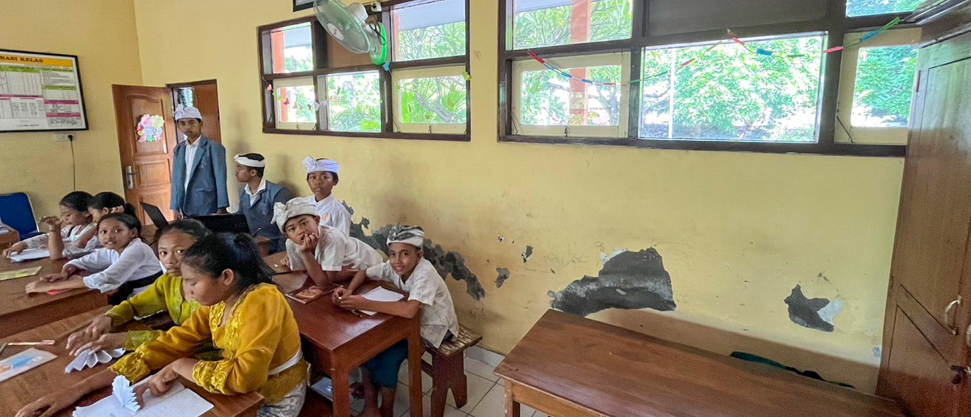 Schoolchildren sit at wooden desks drawing in a classroom with fresh yellow walls.