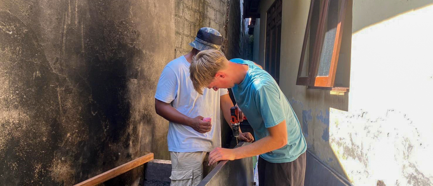 A volunteer drills a board onto a blackened wall as a local builder looks on.
