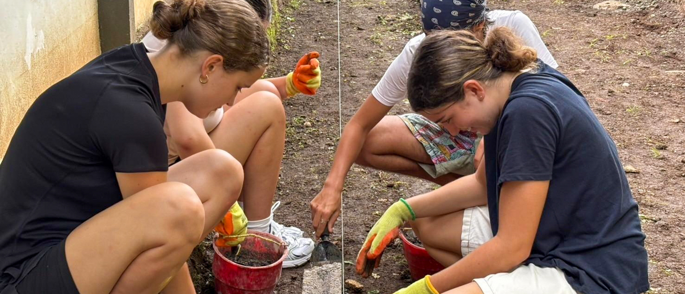 Three volunteers crouch with buckets of cement, setting stones along the edge of a school path.