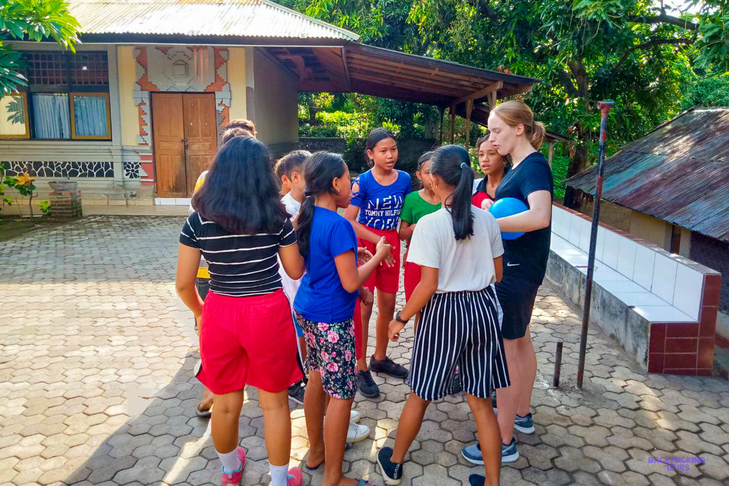A volunteer holds a blue ball as she talks with a group of girls in the schoolyard.